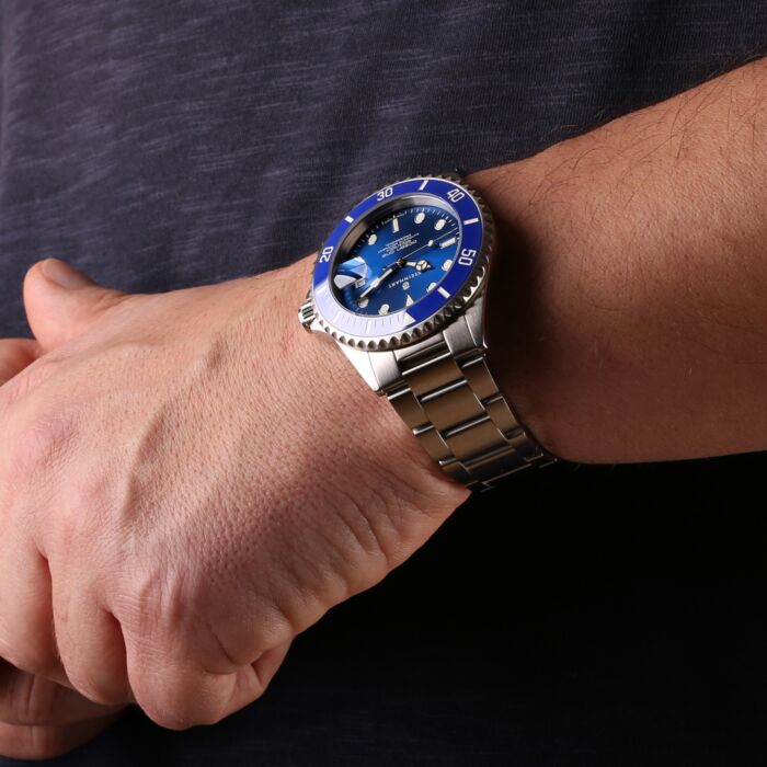Ein Handgelenk mit einer hochwertigen Taucheruhr mit blauem Zifferblatt und Keramikl&uuml;nette. Die Edelstahlarmbanduhr hat ein markantes Design mit leuchtenden Indexen und robustem Geh&auml;use.